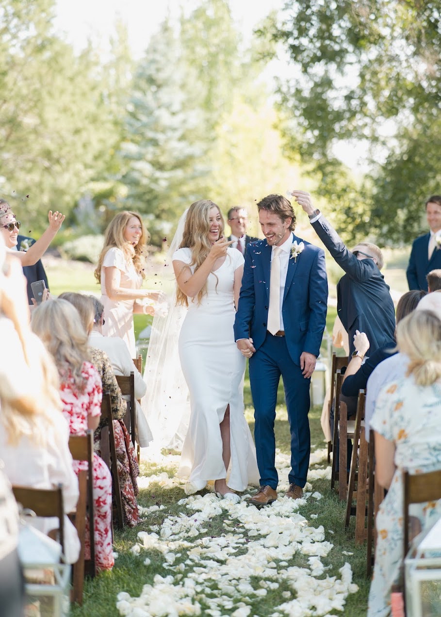 Bride and groom walk down the aisle at an outdoor Idaho summer wedding ceremony with rose petals