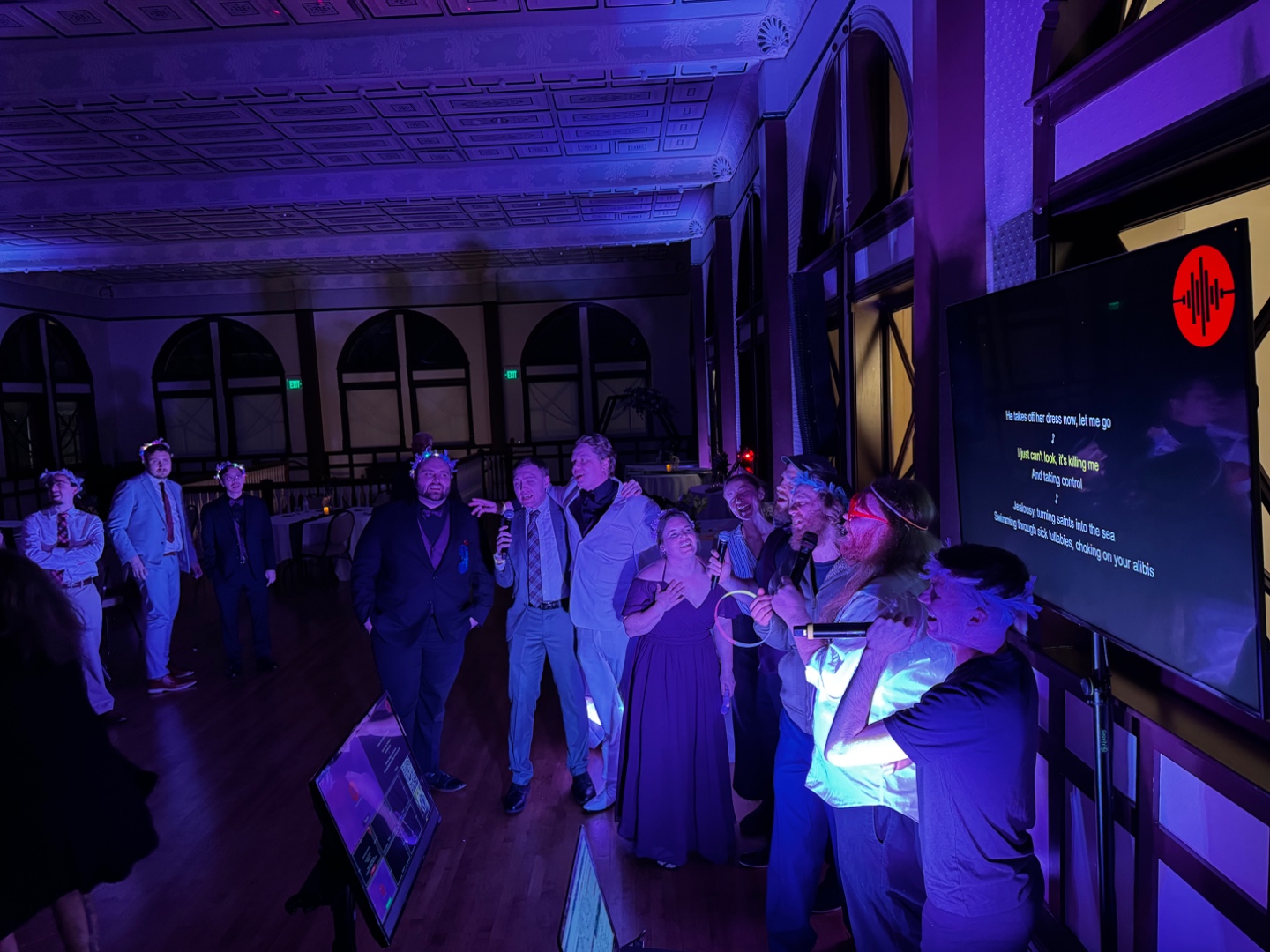 Wide view of a ballroom karaoke event with full group singing and large display screen, SwissMixx Audio