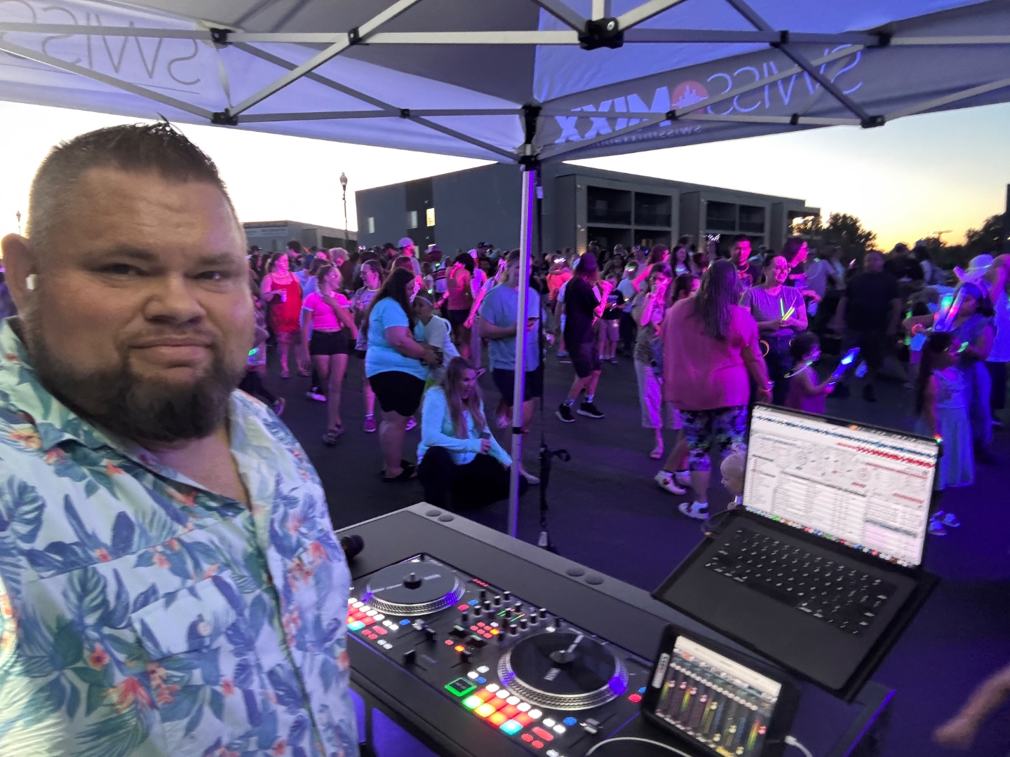 Mark Christiansen DJing at a packed outdoor glow event under the SwissMixx Audio tent with a massive crowd lit in purple and pink, Treasure Valley Idaho live event