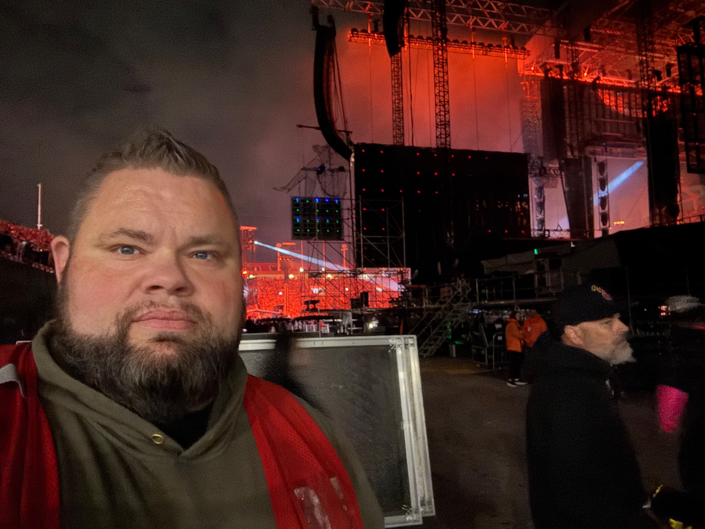 Mark Christiansen backstage during the Post Malone live show with the massive LED stage and packed crowd visible behind him, SwissMixx Audio stadium production