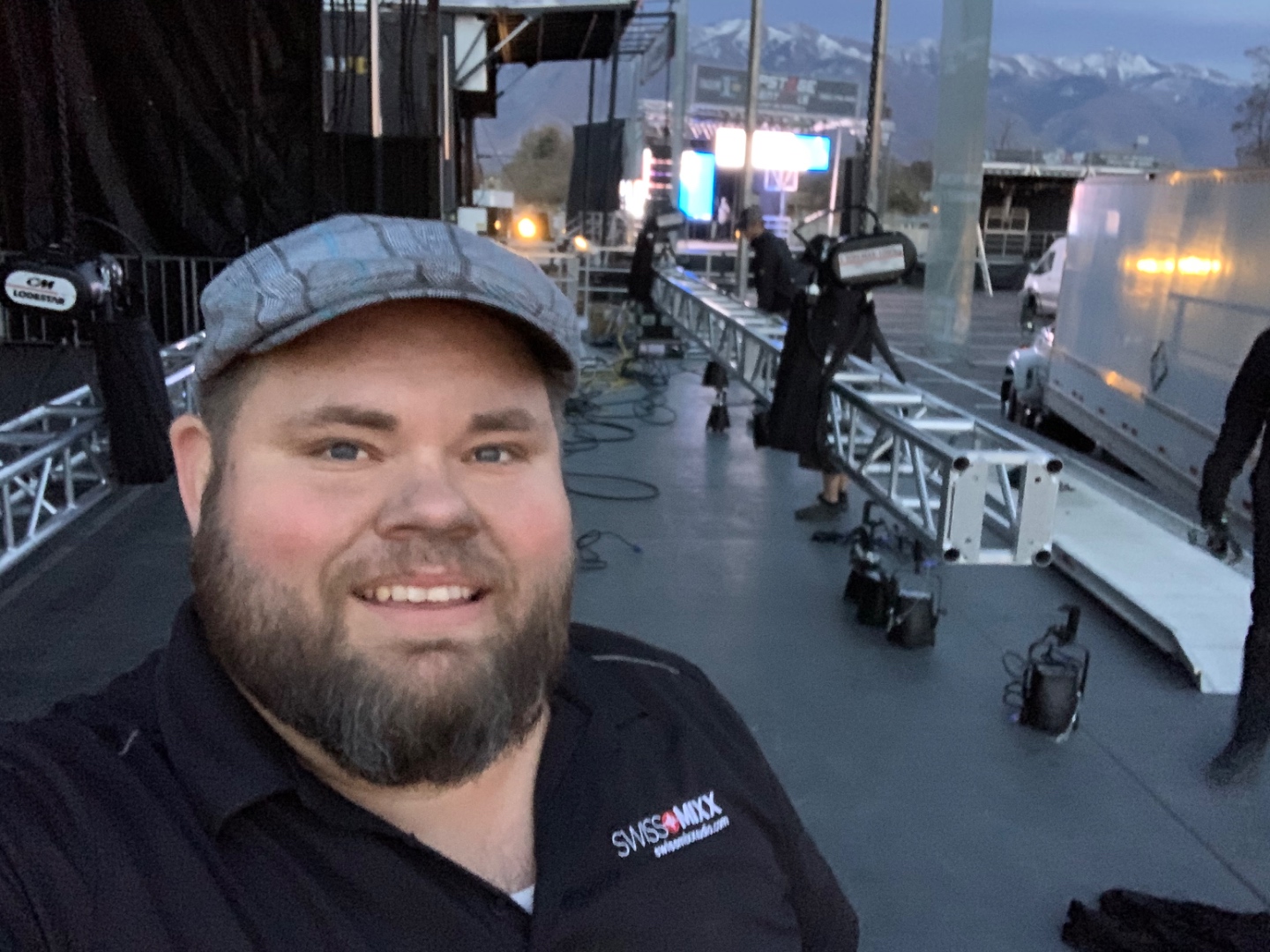 Mark Christiansen on stage during a major outdoor stadium production load-in with snow-capped mountains in the background, SwissMixx Audio live event sound Idaho Utah
