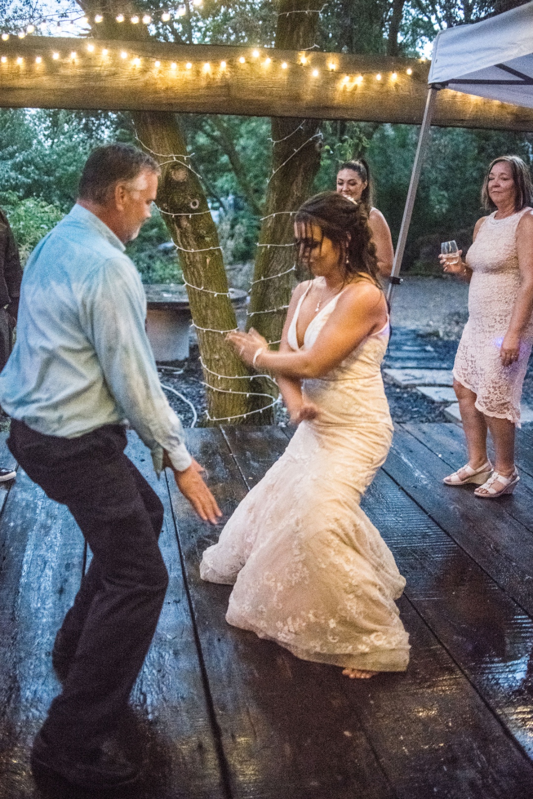 Bride dancing with guests outdoors at Idaho wedding reception with string lights and DJ lighting
